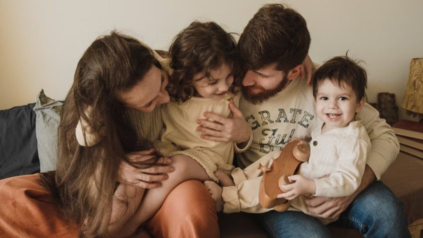 A joyful family moment with parents and children embracing and laughing together indoors.